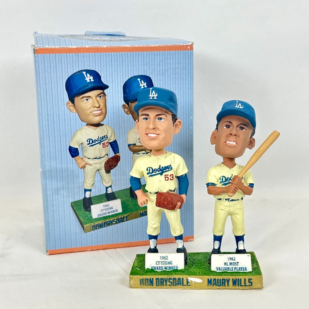 Two baseball bobblehead figurines displayed in front of their original packaging on a light gray background. 