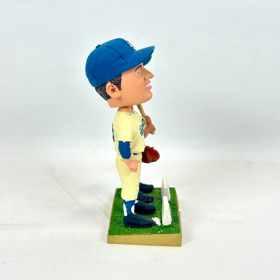 A vintage-style painted bobblehead figurine of a baseball player in a cream and blue uniform with a blue cap.
