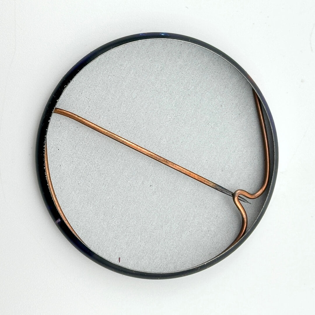 Round metallic object with a copper-colored rod on a white background