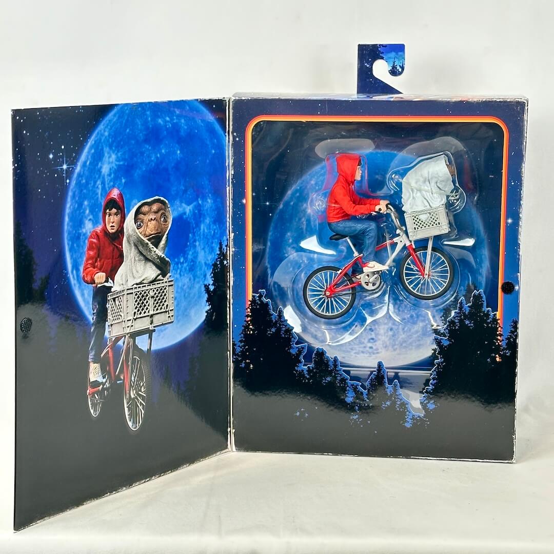 Toy figure of a person on a bike with a dog in a basket against a moonlit sky background