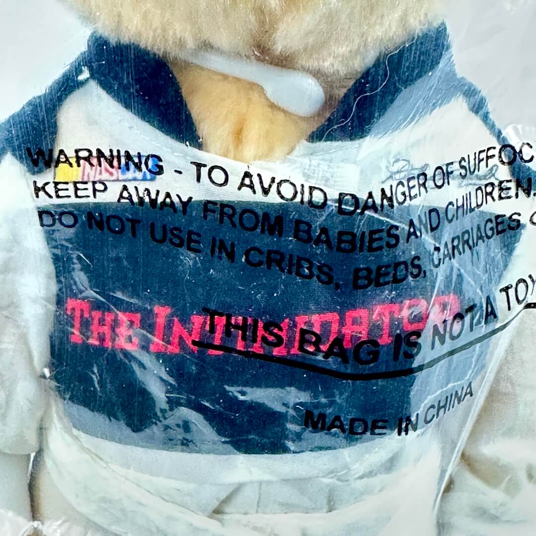 Teddy bear wrapped in plastic with warning labels on a white background