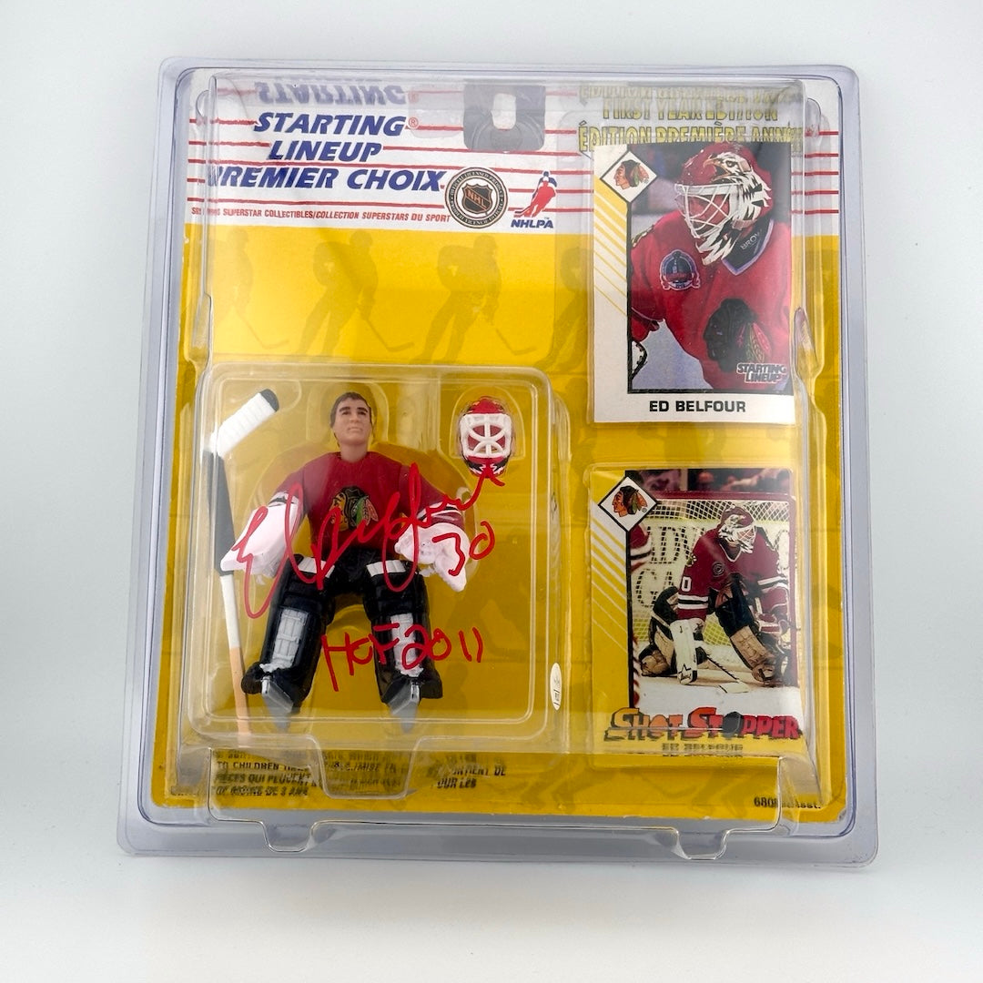 Plastic action figure in Redskins jersey holding hockey stick with red marker signature across front, Ed Belfour HOF 2011.