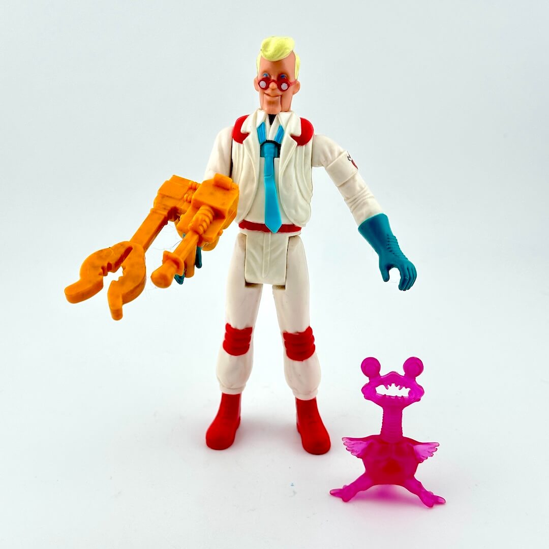 Toy figure in a lab coat with a large orange tool, standing next to a small pink object on a white background