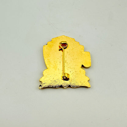 A gold-colored enamel pin shown from the back, featuring a stylized silhouette with a safety pin clasp.