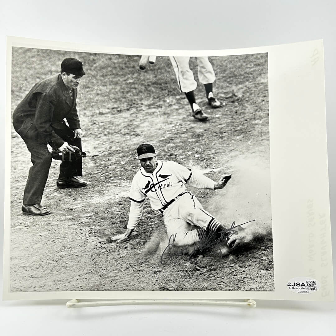 Vintage black and white photograph of a baseball player sliding into home plate with an umpire and another player in the background.