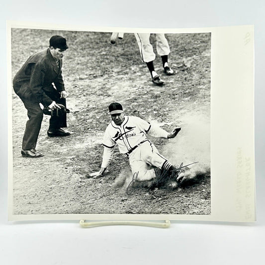 Vintage black and white photograph of a baseball player sliding into home plate with an umpire and another player in the background.