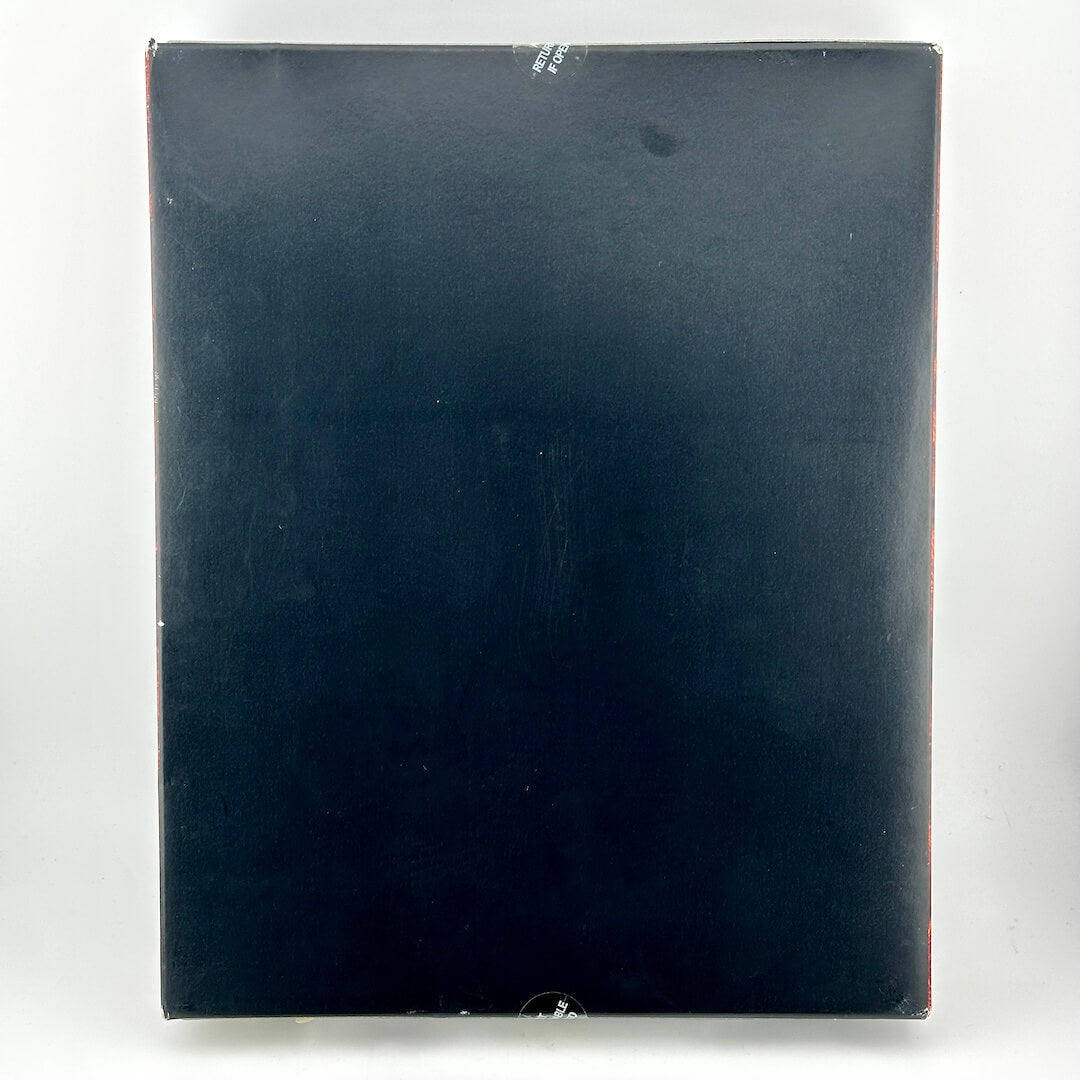 The back of a black rectangular product box, showing a plain matte black surface with a small white sticker near the top.