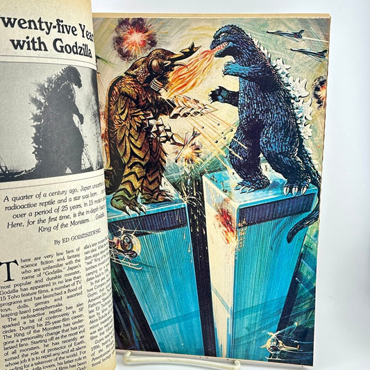 An open vintage magazine spread showing a colorful illustration of a monster breathing fire onto Godzilla.