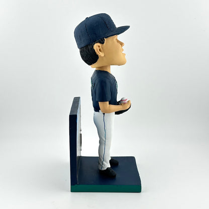 Bobblehead of a baseball player in a blue uniform with a cap, holding a ball, on a white background.