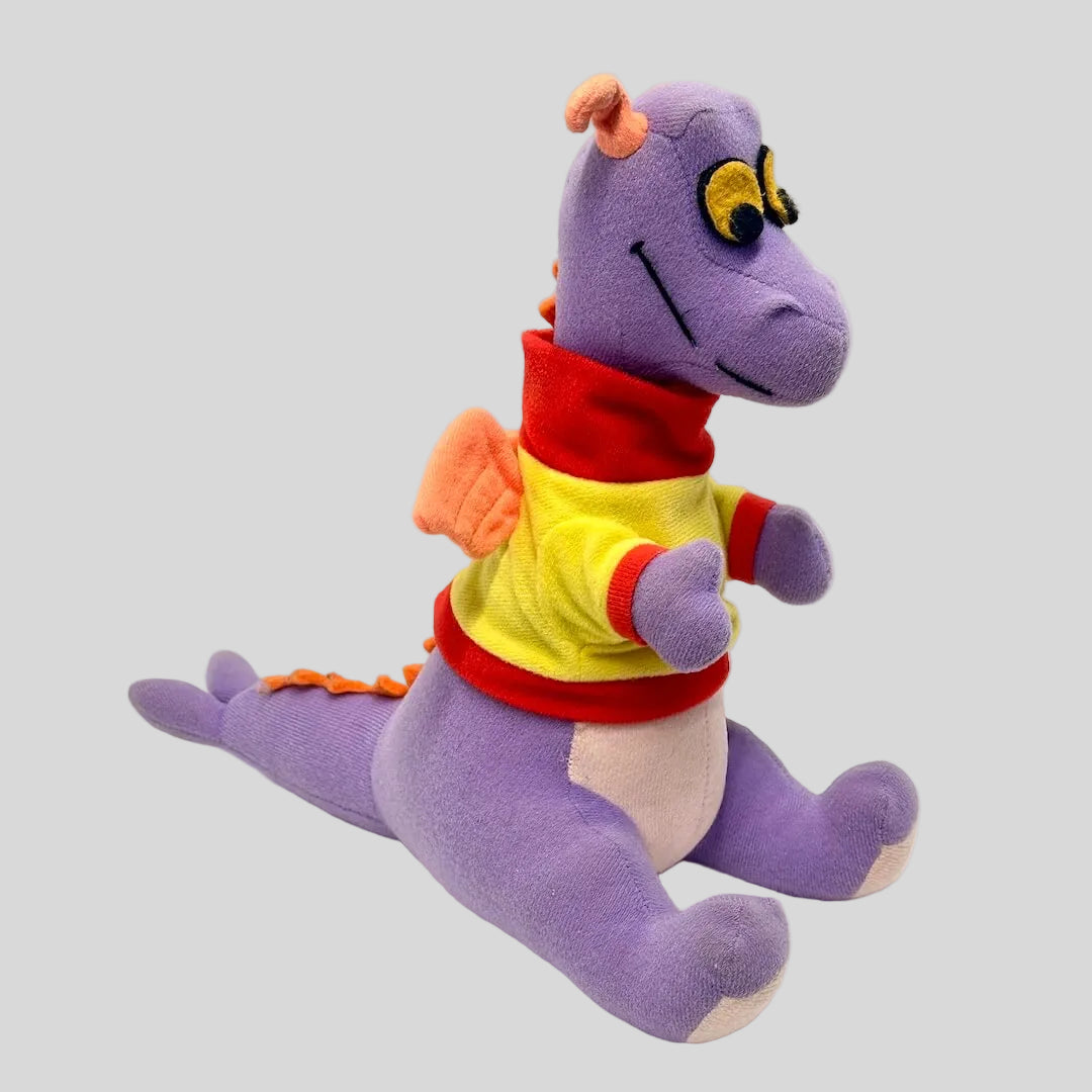 Purple dinosaur plush toy wearing a colorful shirt on a white background
