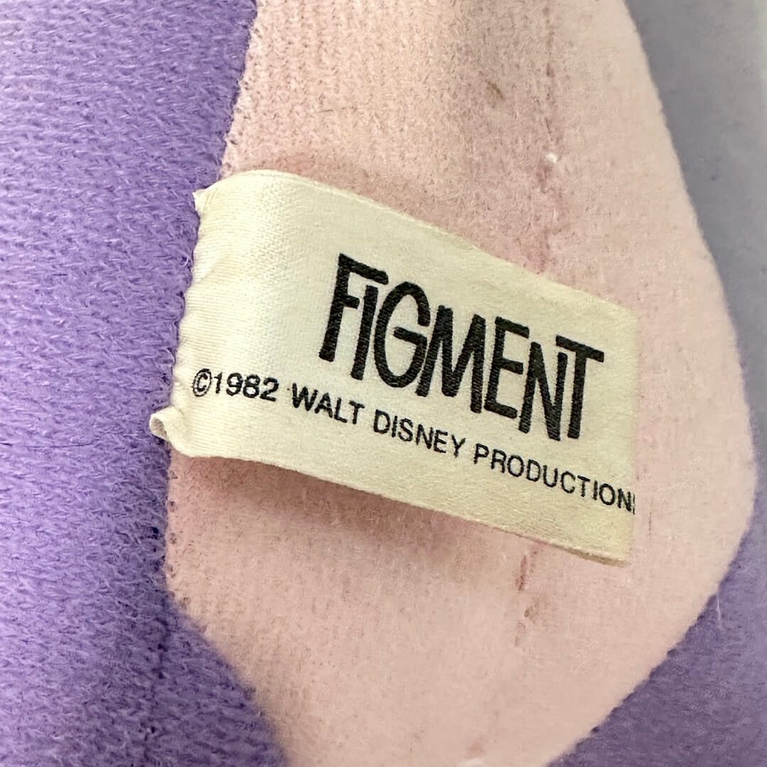 Label on a plush toy with 'Figment' and 'Walt Disney Productions' text, set against a purple and gray background.