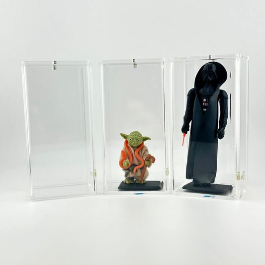 Two action figures, one green and one black, in a clear display case next to one empty case on a white background.