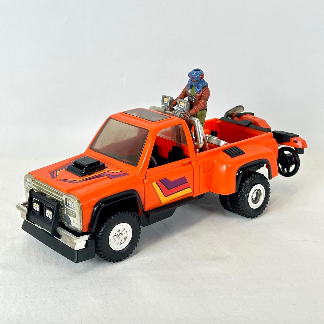 An orange toy pickup truck with purple and yellow graphic accents, featuring a small driver figure and a attached motorcycle.