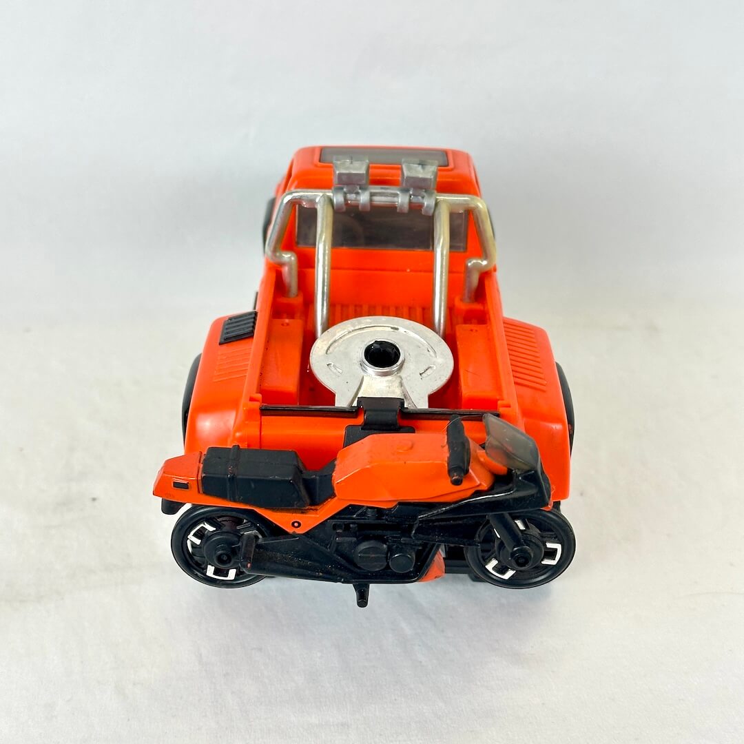 An orange toy pickup truck with a small black and orange motorcycle attached to the back.