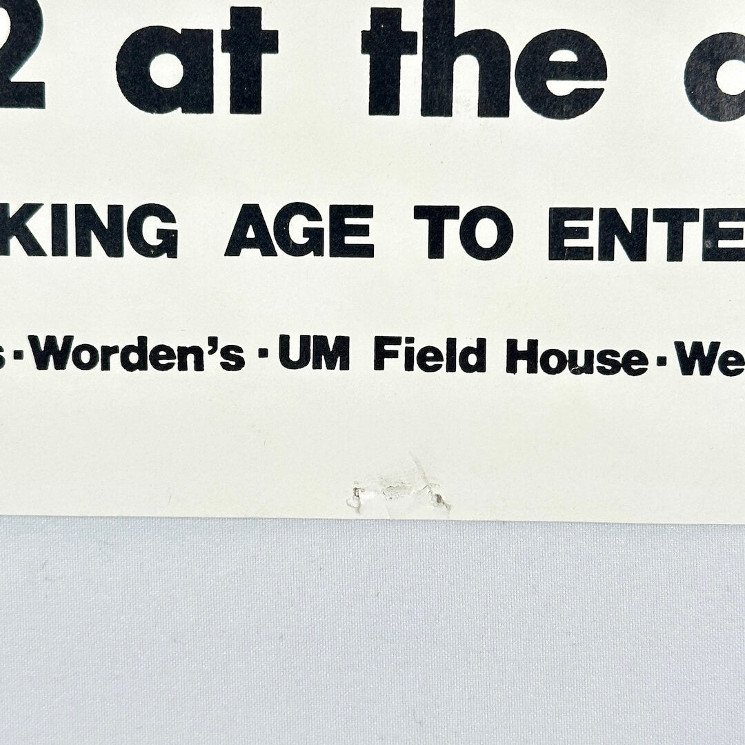 Bottom center of poster with pin holes. 