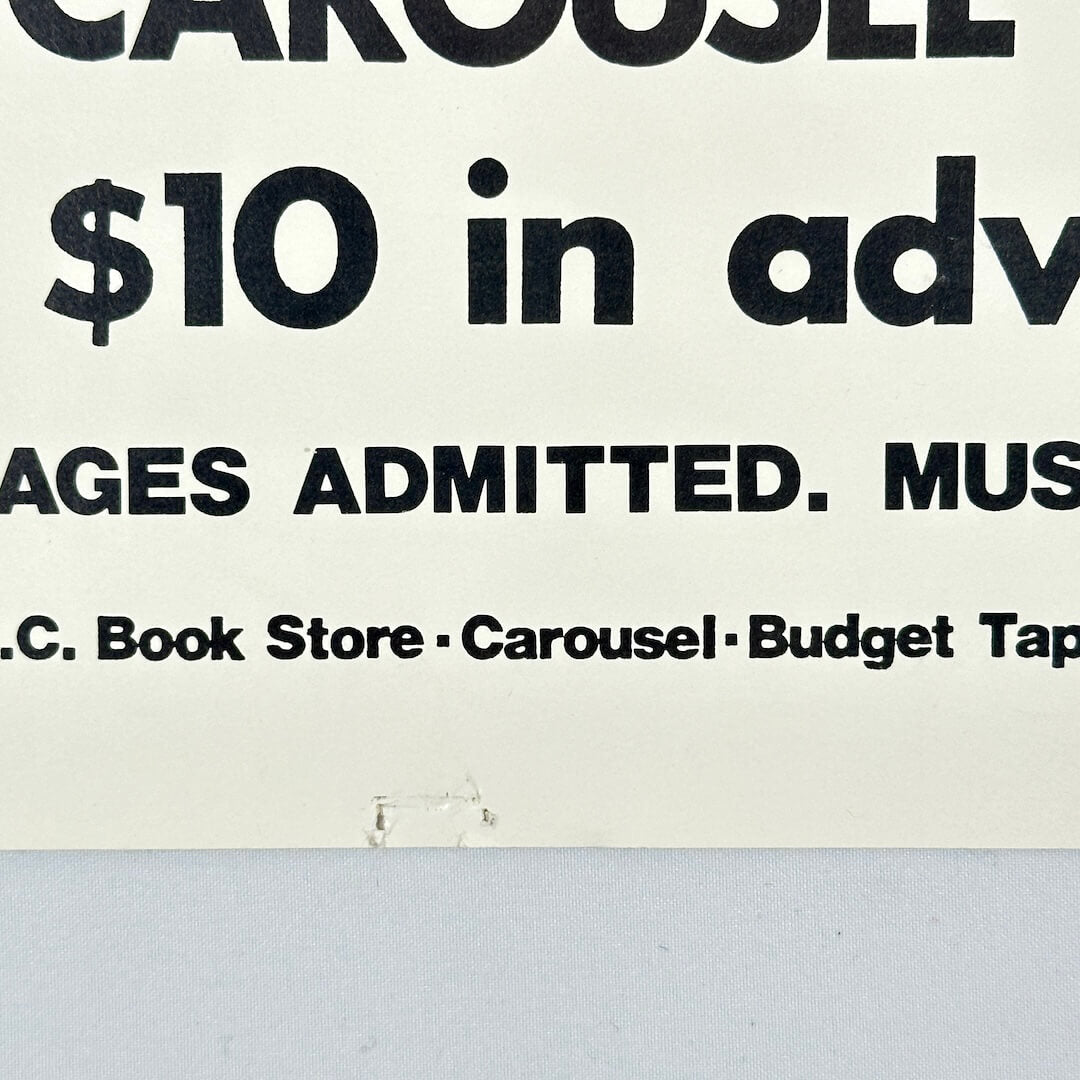 Bottom center of poster with pin holes. 