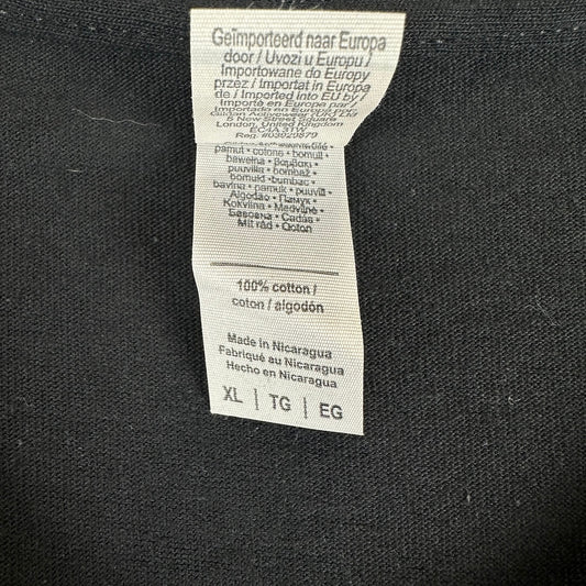 A close-up of a white fabric care label sewn onto black knit clothing.