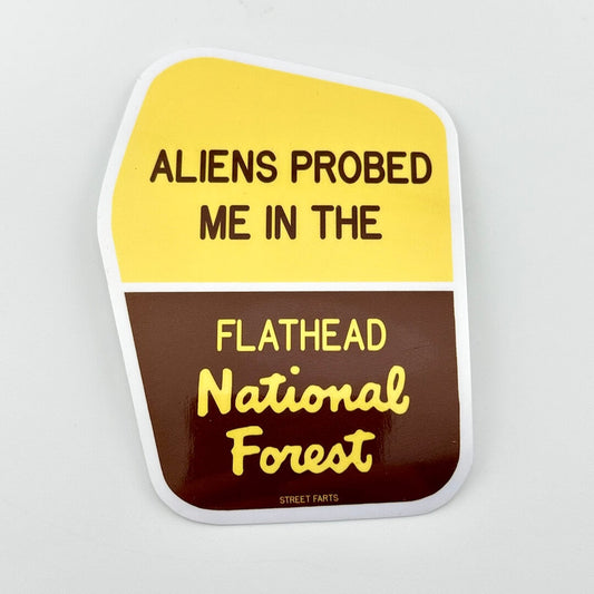 Sticker with text 'ALIENS PROBED ME IN THE FLATHEAD National Forest' on a yellow and brown background