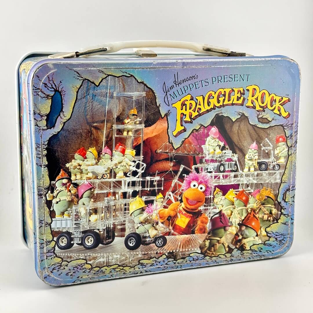 Vintage metal lunchbox with images from Fraggle Rock in color on side with wear along edges. 