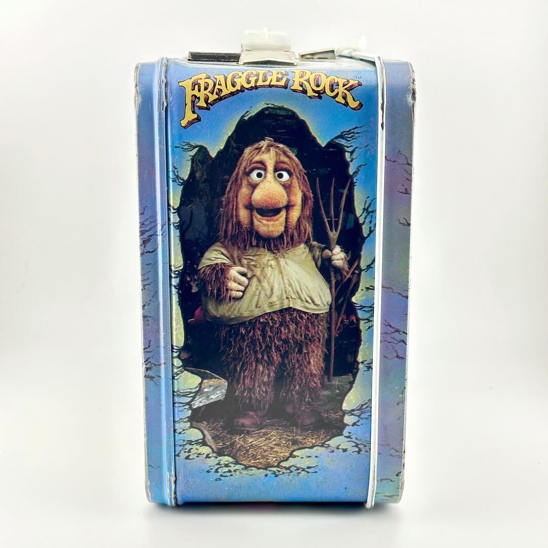 Side view of vintage metal lunchbox with image of character from Fraggle Rock under show logo. 