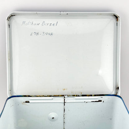 View of interior lid of metal lunchbox showing a name and number written in pen and etched into lid. 