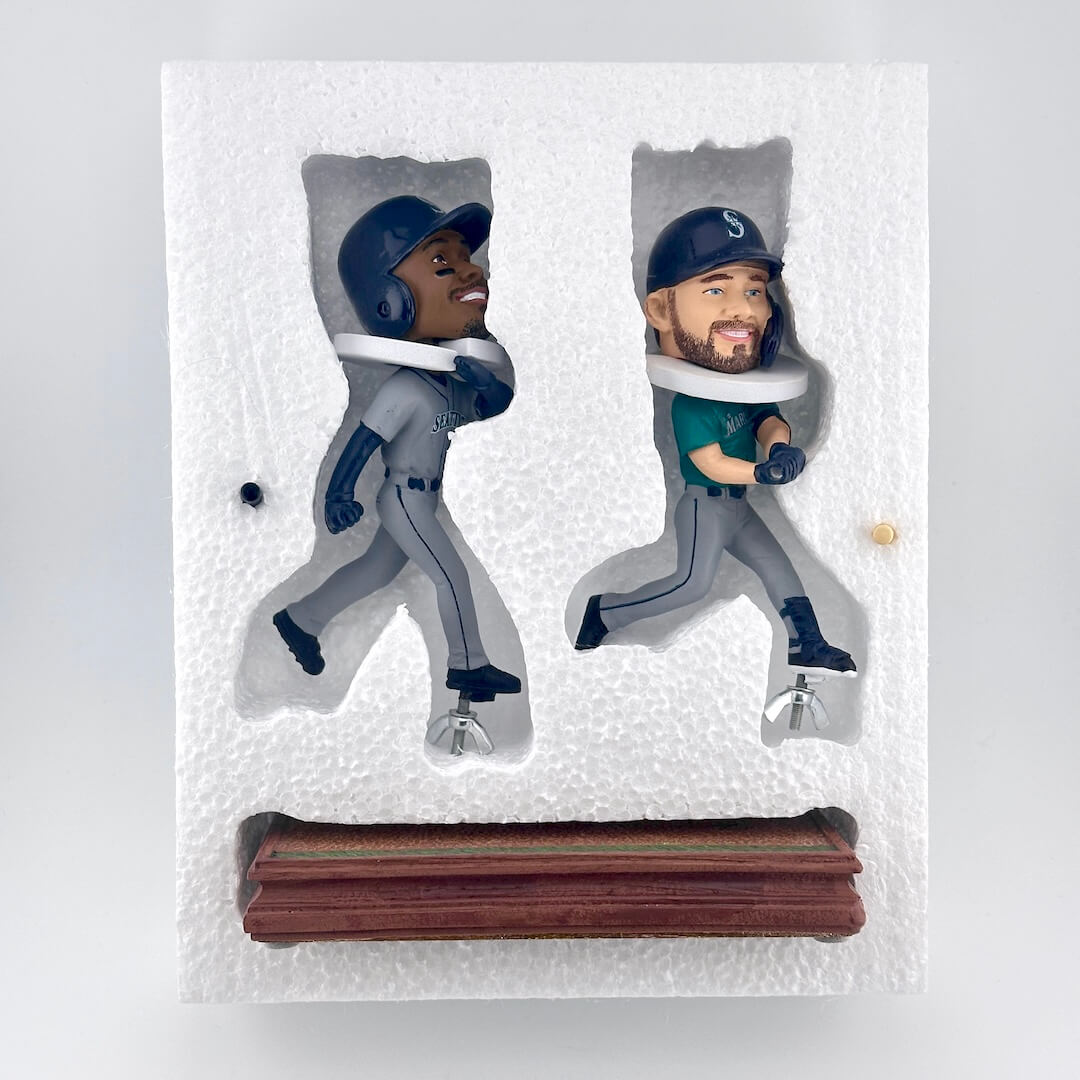 bobbleheads of two baseball players in Seattle Mariners uniforms, mounted in a white foam backing with a wooden base.