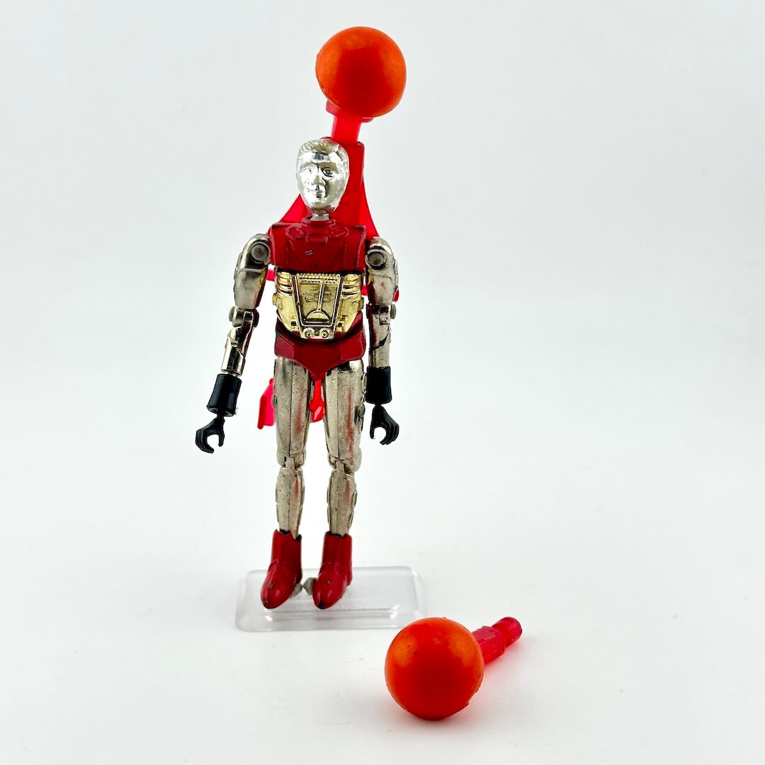 Silver and red humanoid action figure with red pack and orange missile accessory standing against white background. 