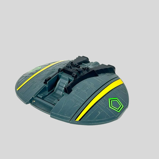 A toy spaceship accessory in dark gray-green with bright yellow stripes and a green hexagonal emblem.