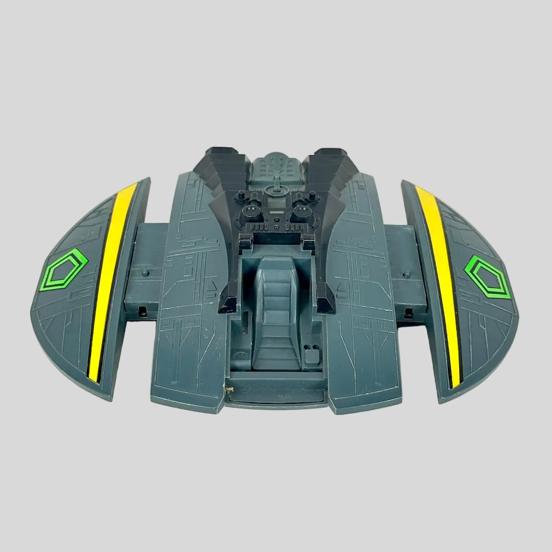 A toy spaceship accessory in dark gray-green with bright yellow stripes and a green hexagonal emblem.