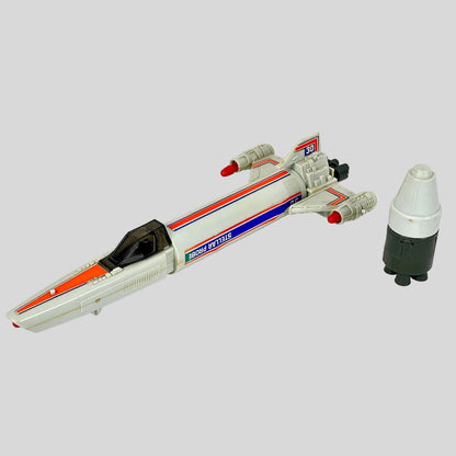 A vintage toy spaceship model shown alongside a matching white, gray, and black capsule accessory. 