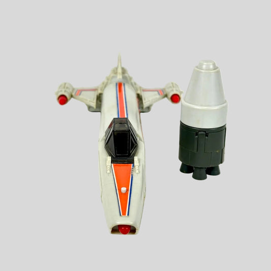 A vintage toy model of a sci-fi spaceship, shown alongside a matching cylindrical booster on a plain background.