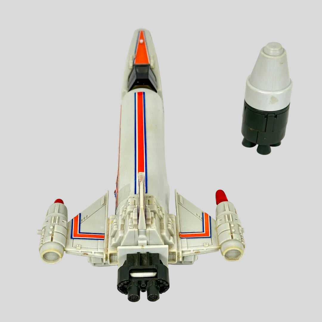 A vintage toy model spacecraft, shown from a top-down perspective alongside its matching white, gray, and black accessory.