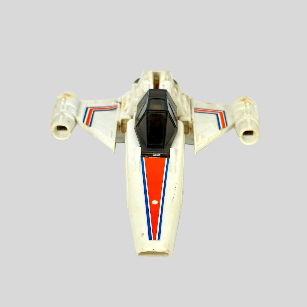 A vintage toy model of a white futuristic spacecraft, featuring red and blue stripes on the nose and wings, with a black cockpit canopy.