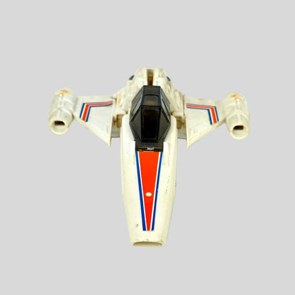A vintage toy model of a white futuristic spacecraft, featuring red and blue stripes on the nose and wings, with a black cockpit canopy.