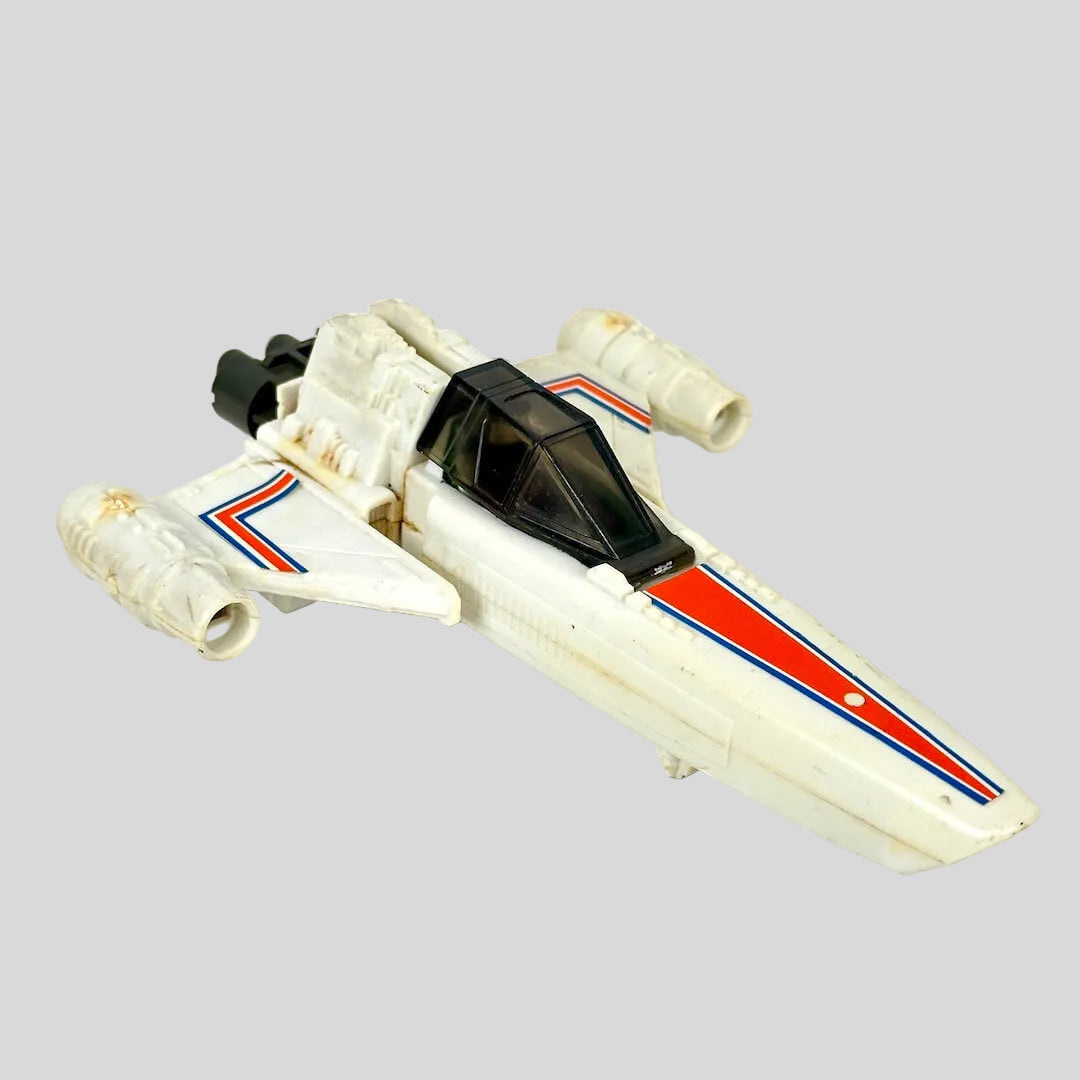 A vintage white toy spacecraft with orange and blue stripes, photographed on a light off-white background.