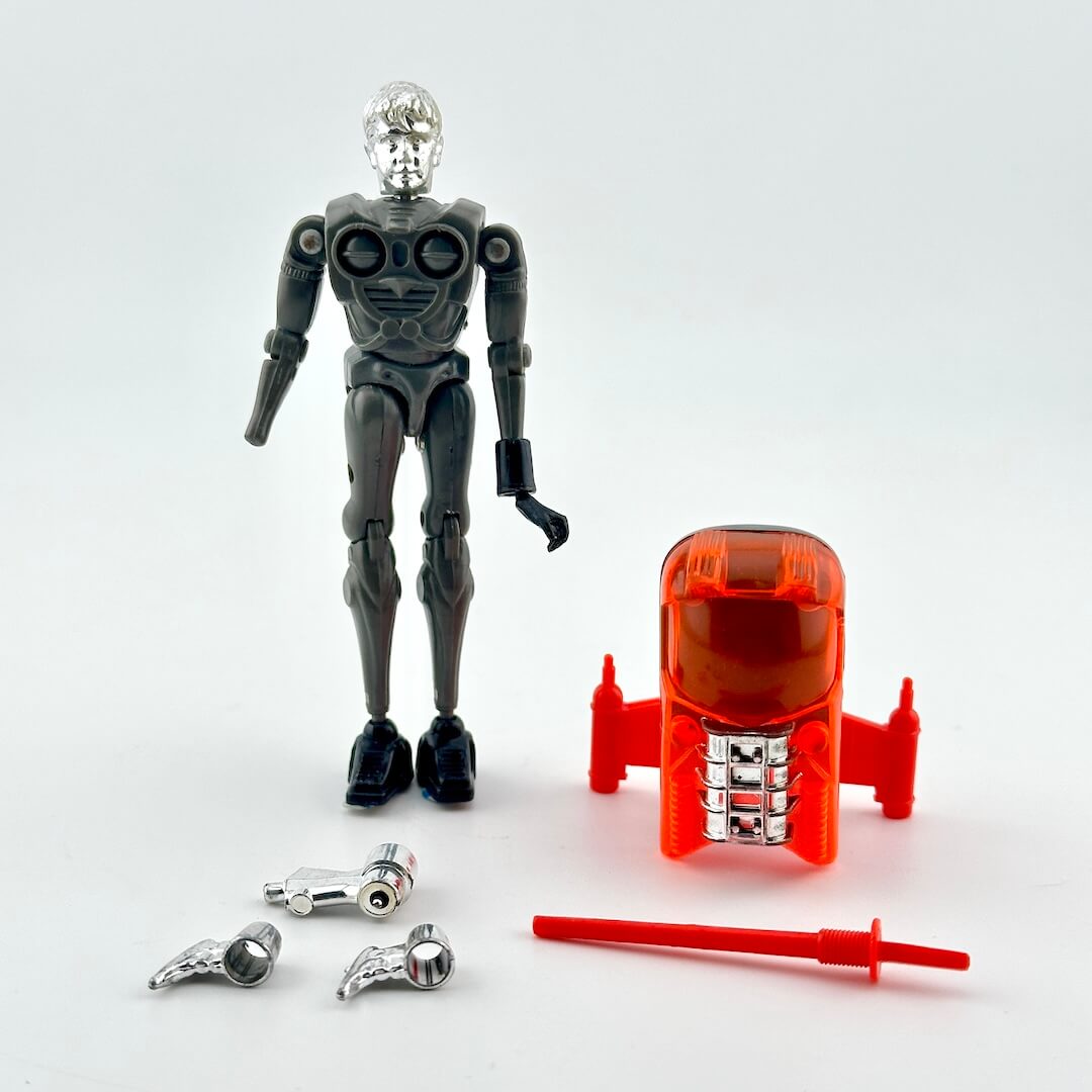 A toy silver robot standing next to a red vehicle accessory, with two silver weapon pieces and a red sword placed in front.