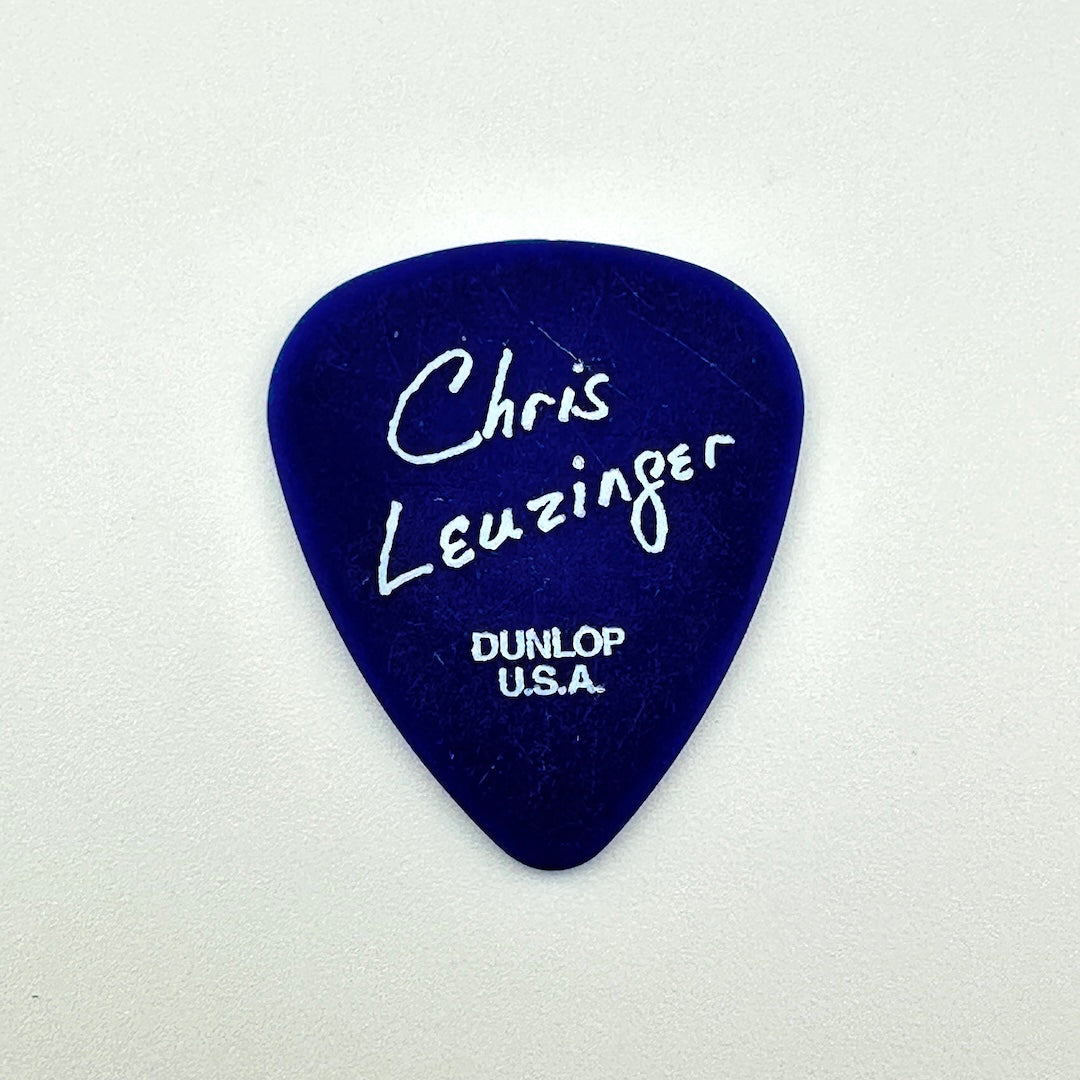A dark blue guitar pick with white handwritten text reading 'Chris Leuzinger' and 'DUNLOP U.S.