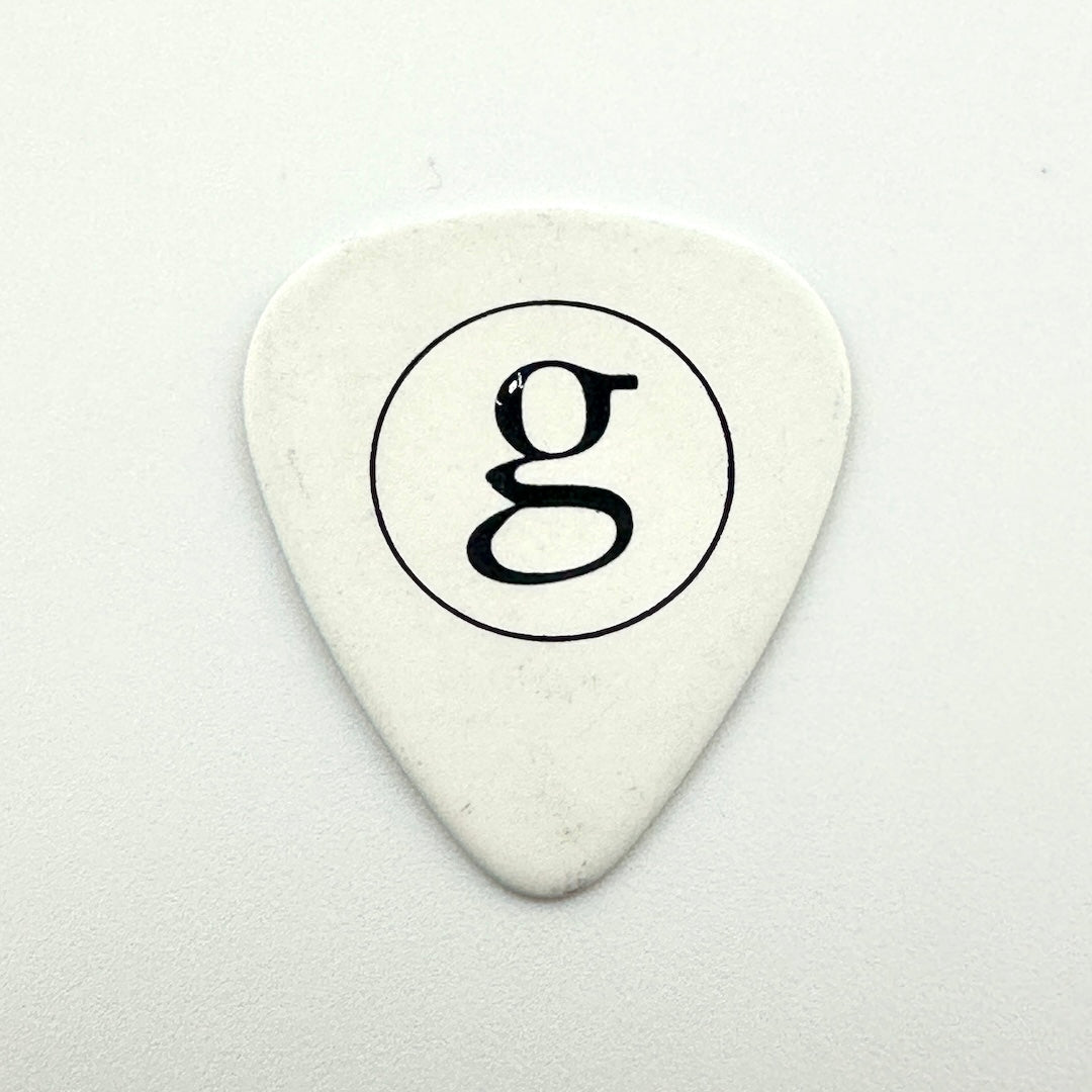 White guitar pick with silver 'g' in circle set against a white background. 