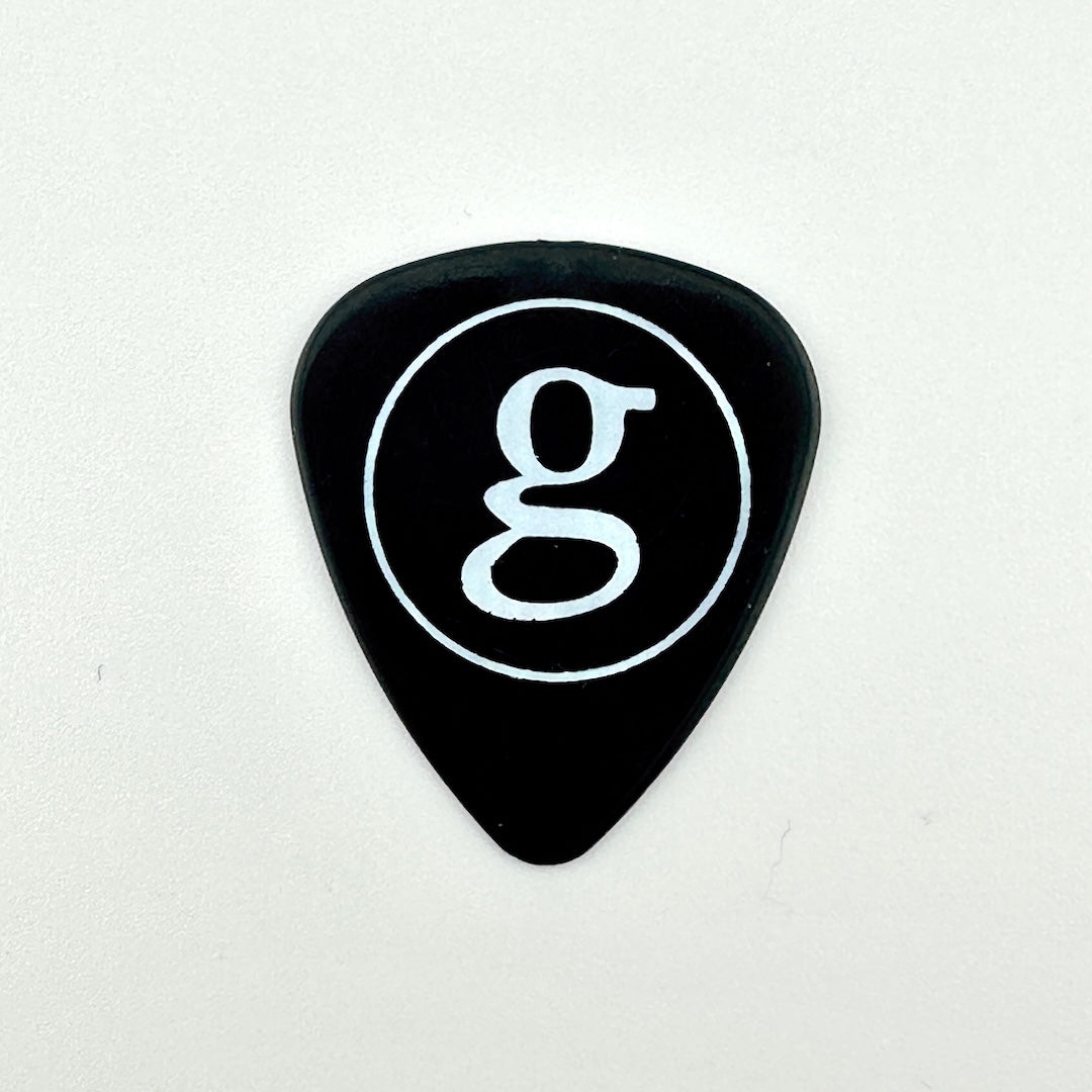 A black guitar pick with a white circular logo containing a lowercase 'g' in the center, set against a white background.