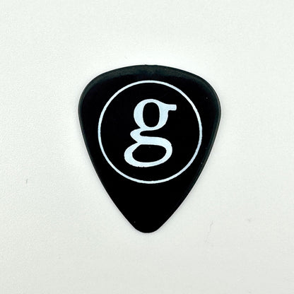 A black guitar pick with a white circular logo containing a lowercase 'g' in the center, set against a white background.