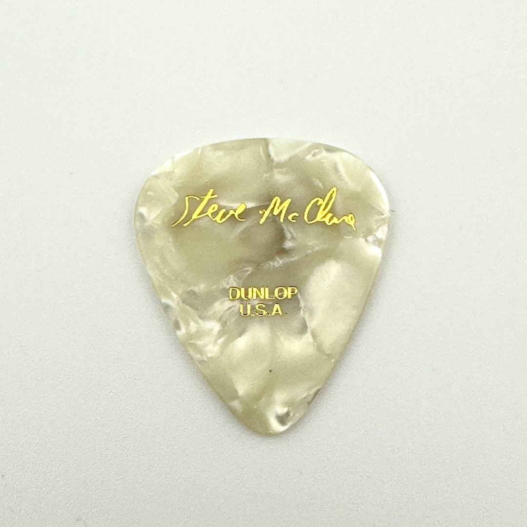 A pearlescent off-white guitar pick with gold foil lettering reading 'Steve McClure' and 'DUNLOP USA'.