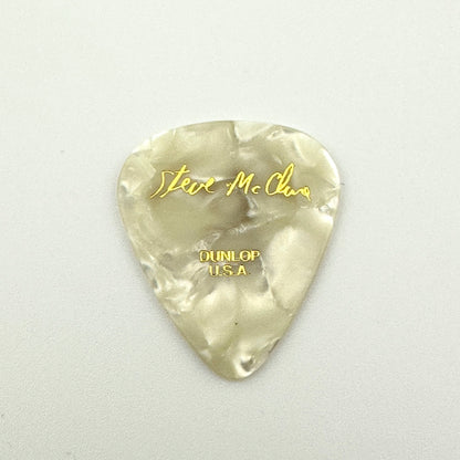A pearlescent off-white guitar pick with gold foil lettering reading 'Steve McClure' and 'DUNLOP USA'.
