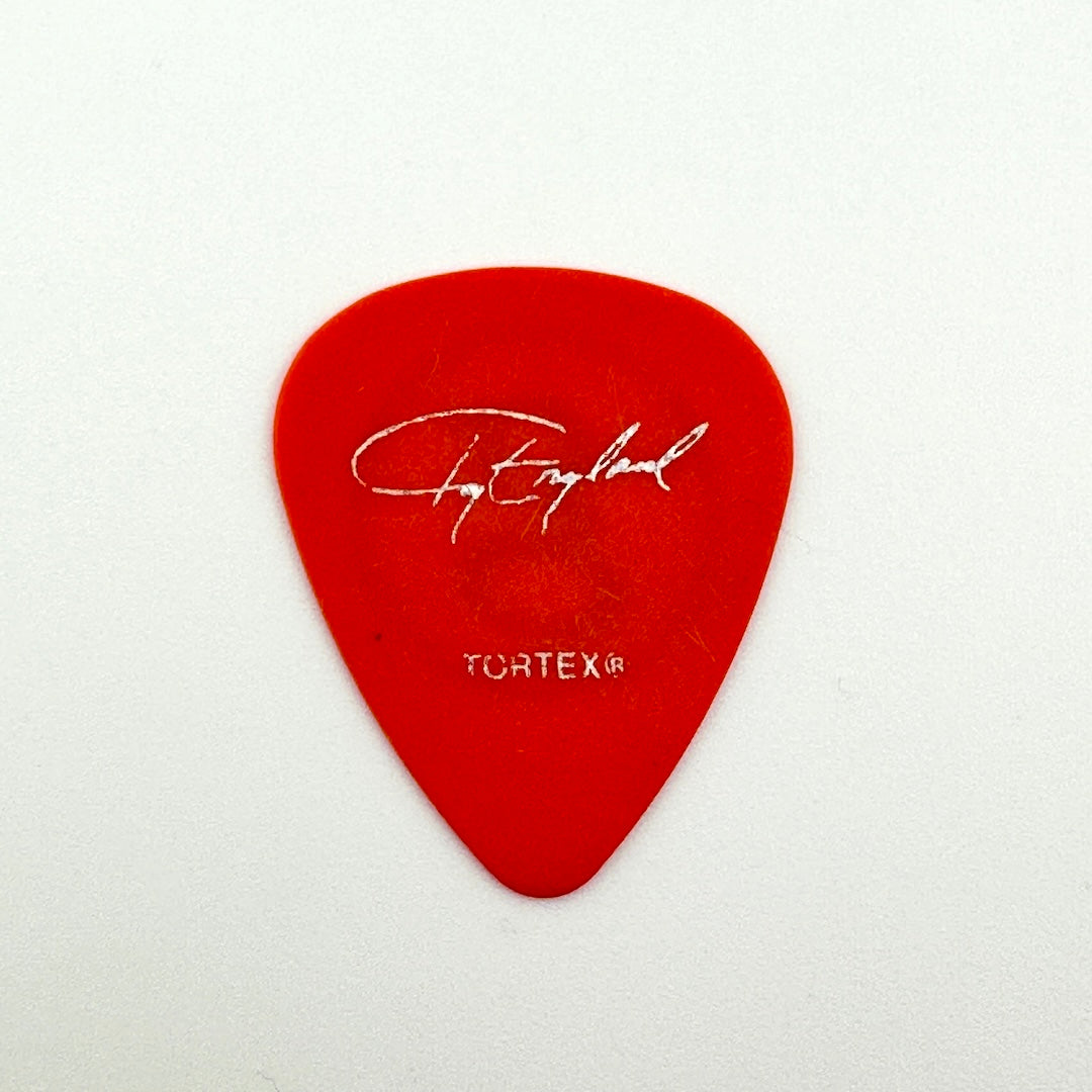 A single red guitar pick with a white signature logo and 'TORTEX' text, photographed on a plain white background.