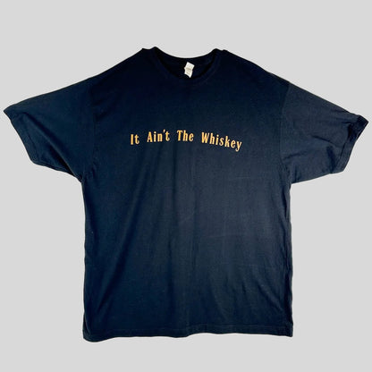 A black short-sleeve t-shirt with the phrase 'It Ain't The Whiskey' printed across the chest in a yellow serif font.
