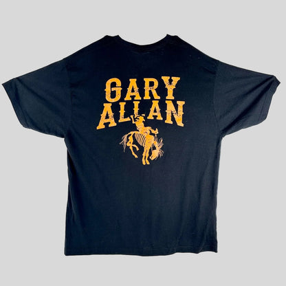 A black short-sleeve t-shirt laid, featuring a distressed yellow graphic that reads 'GARY ALLAN' above a cowboy riding a bucking horse.