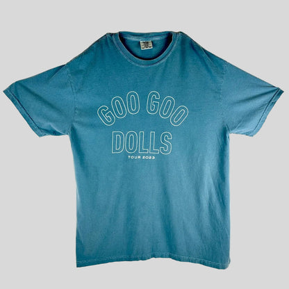 A faded blue short-sleeve t-shirt laid flat, featuring the text 'GOO GOO DOLLS' and 'TOUR 2023' printed in white outline on the front.