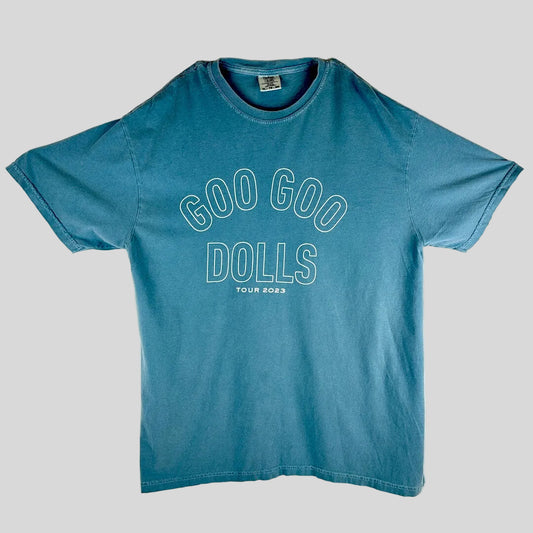 A faded blue short-sleeve t-shirt laid flat, featuring the text 'GOO GOO DOLLS' and 'TOUR 2023' printed in white outline on the front.