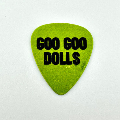 A bright lime green guitar pick with the words 'GOO GOO DOLLS' printed in bold black capital letters, on a white background.