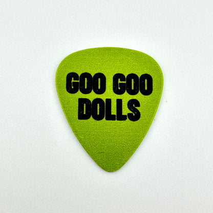 A lime green guitar pick with the text 'GOO GOO DOLLS' printed in bold black letters, centered on a light off-white background.