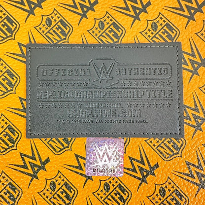 A close-up of a dark gray WWE official authenticating patch on a bright yellow and black patterned surface, with a holographic WWE sticker below it.